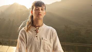 A person meditating on a wooden deck with a mountainous landscape in the background.