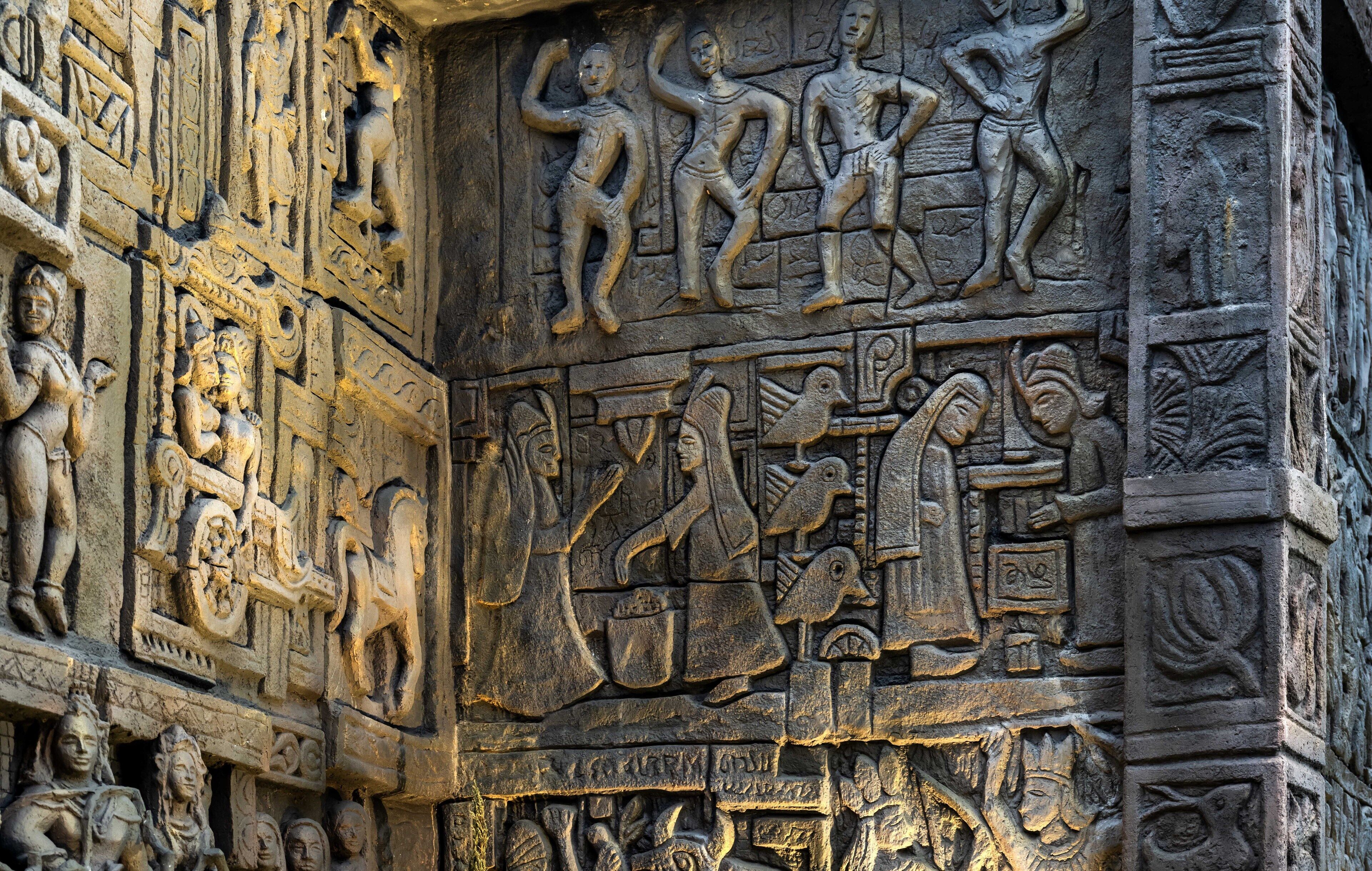 Gedetailleerde stenen beeldhouwwerken op een tempelmuur, waarop verschillende figuren en scènes te zien zijn.