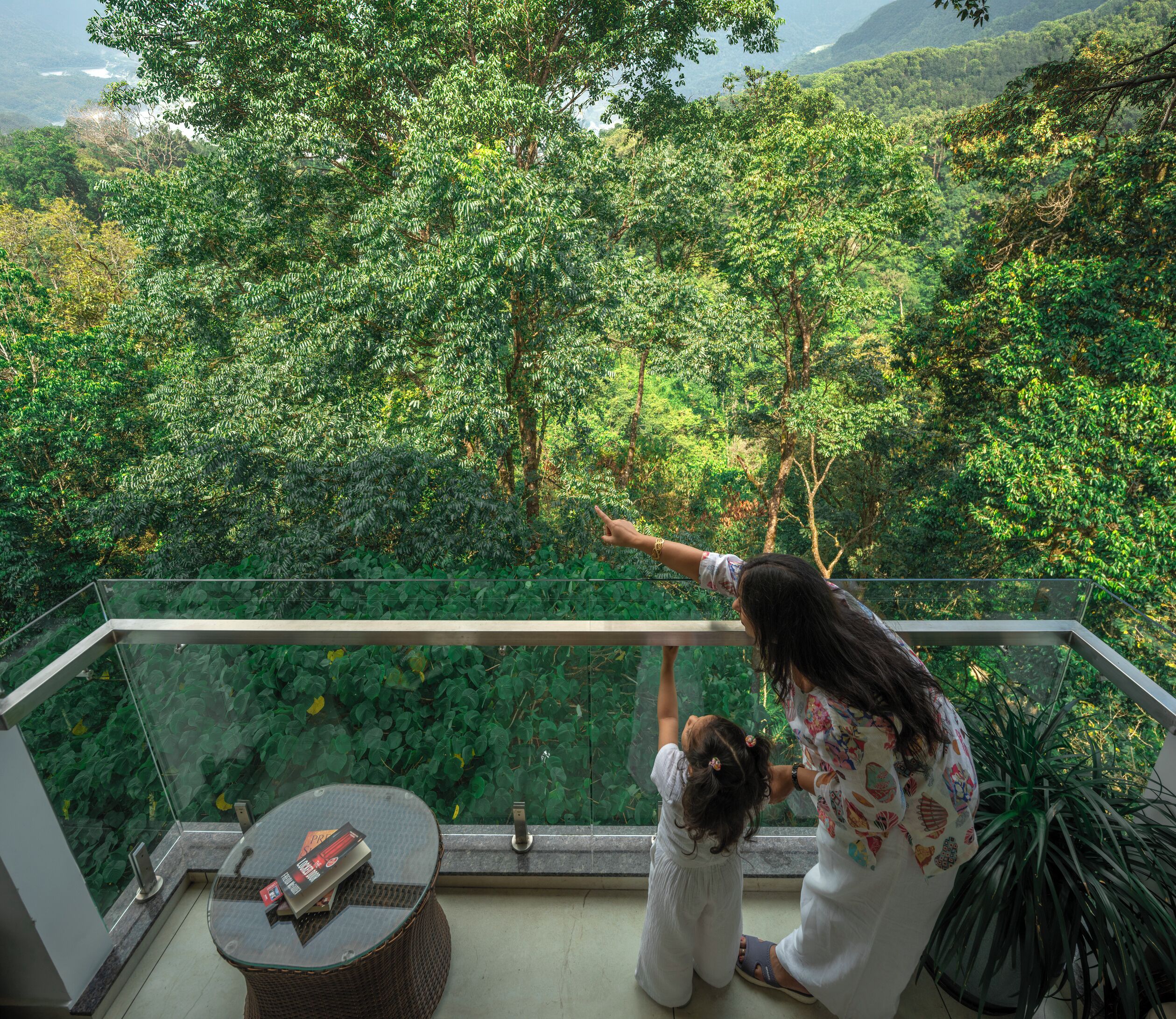Un balcon doté d’une balustrade en verre, offrant une vue sur une forêt verdoyante et luxuriante.