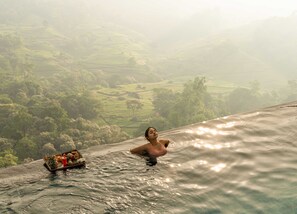 Una persona en el agua con una bandeja de comida y una bebida, rodeada de un paisaje montañoso.