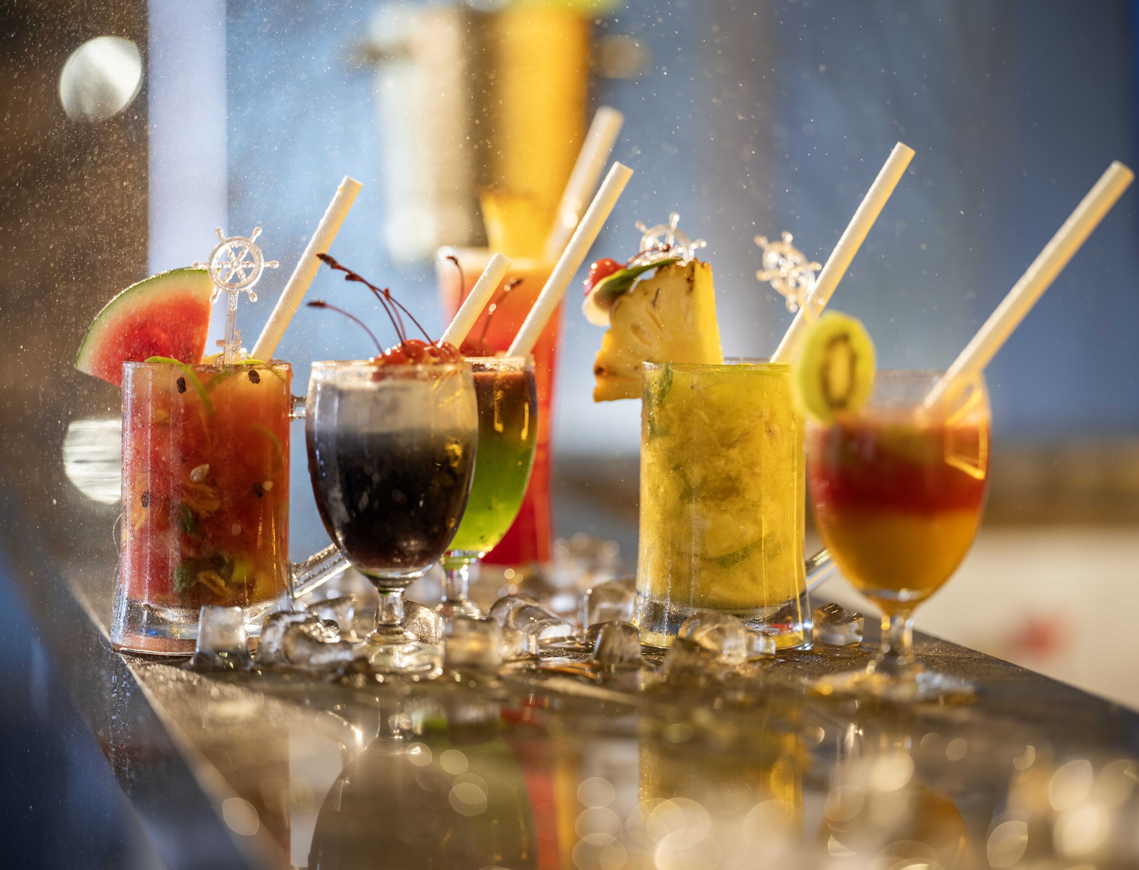 A bar with various colorful cocktails, each with a straw and garnishes.