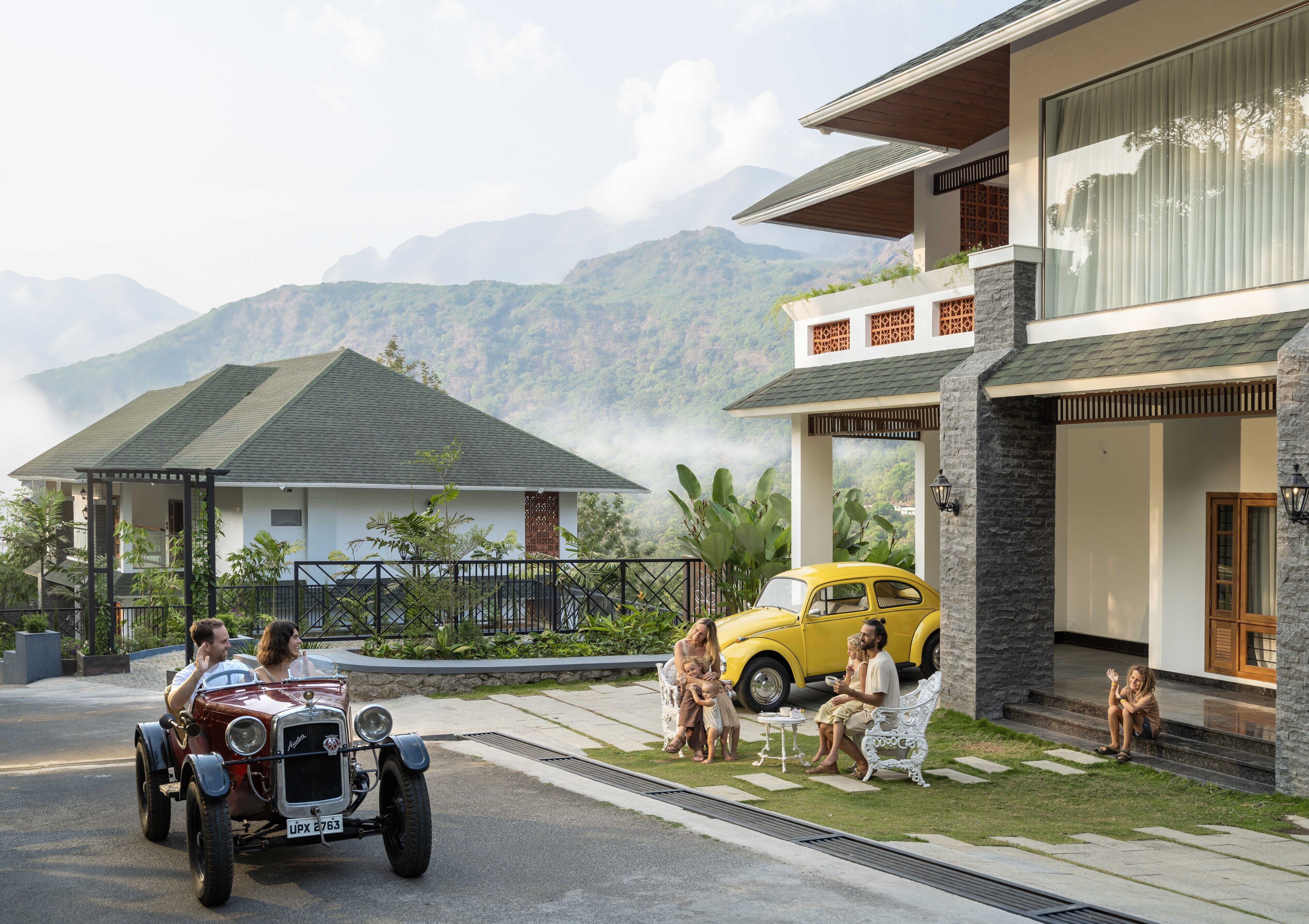 A modern house with a balcony, a yellow car, and a vintage car parked in front.
