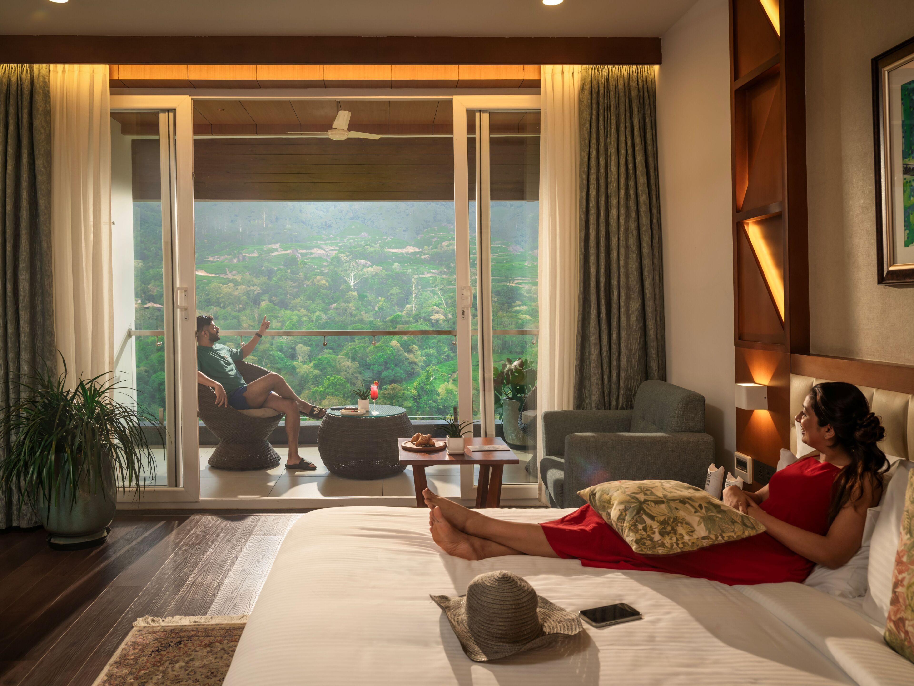 A hotel room with a large bed, a balcony with a view, a sitting area, and a dining table.