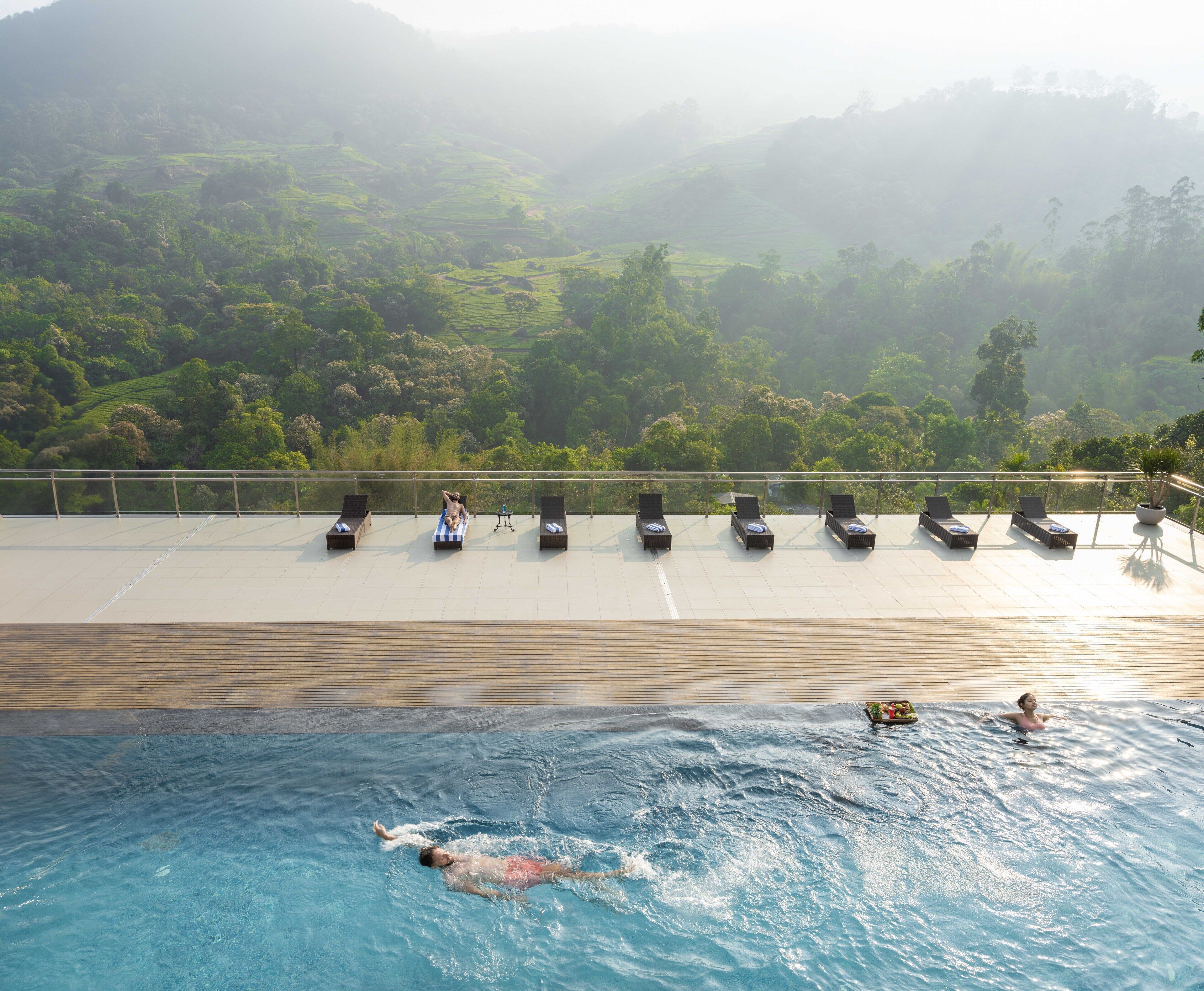 Una piscina con una persona nadando, sillas de descanso y vistas a un paisaje montañoso.