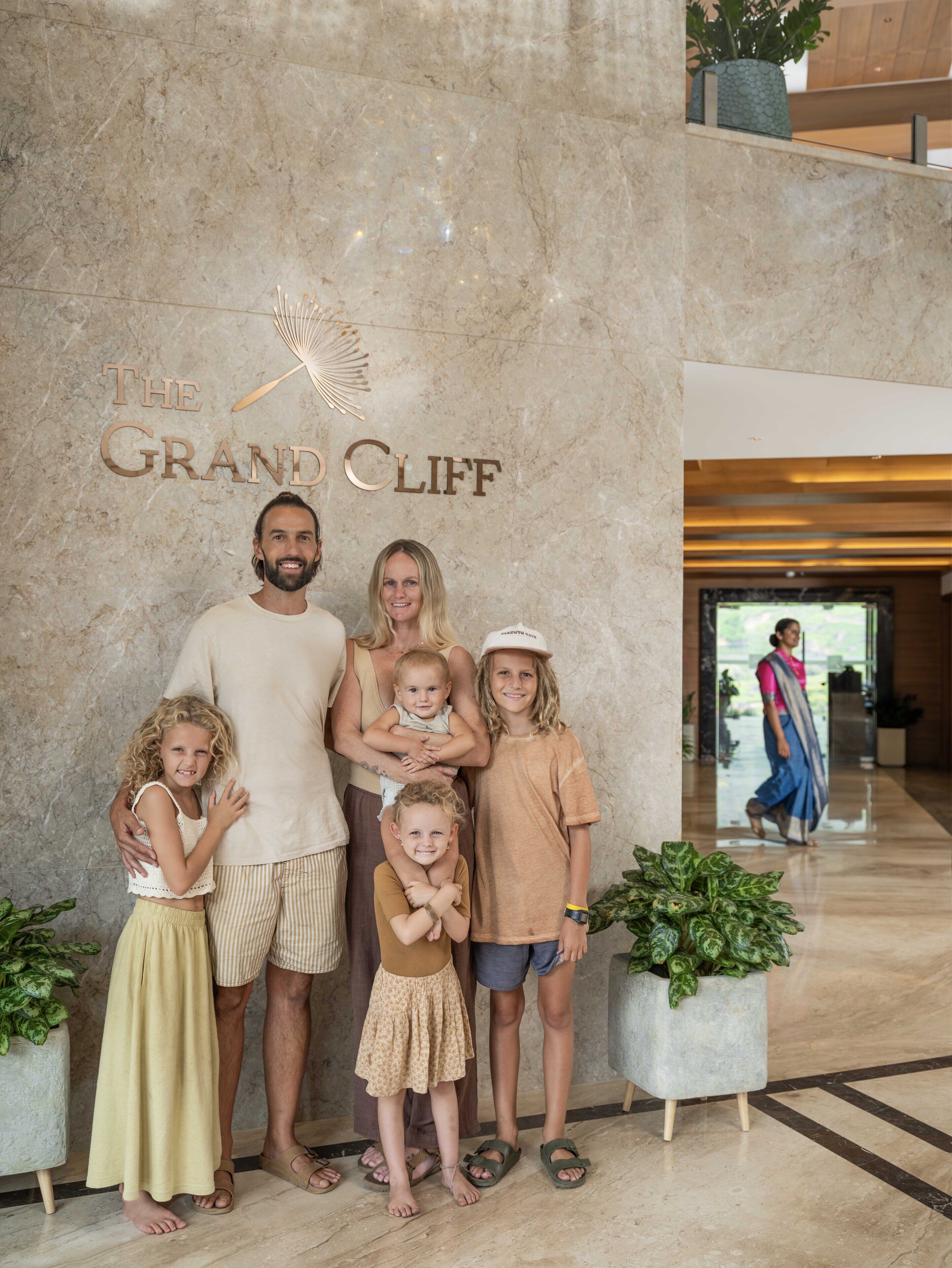 En familie poserer foran en marmorvæg med teksten "The Grand Cliff".