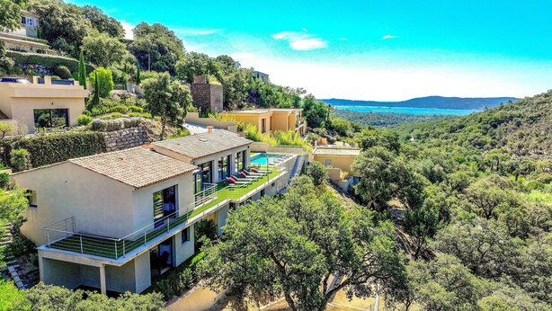 A modern villa with a swimming pool, surrounded by lush greenery and a scenic view of the sea.