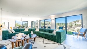 A modern living room with green sofas, a coffee table, and a view of a hillside.