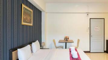 Habitación de hotel con cama, una mesita con un jarrón de flores, una silla y una puerta con un cartel.