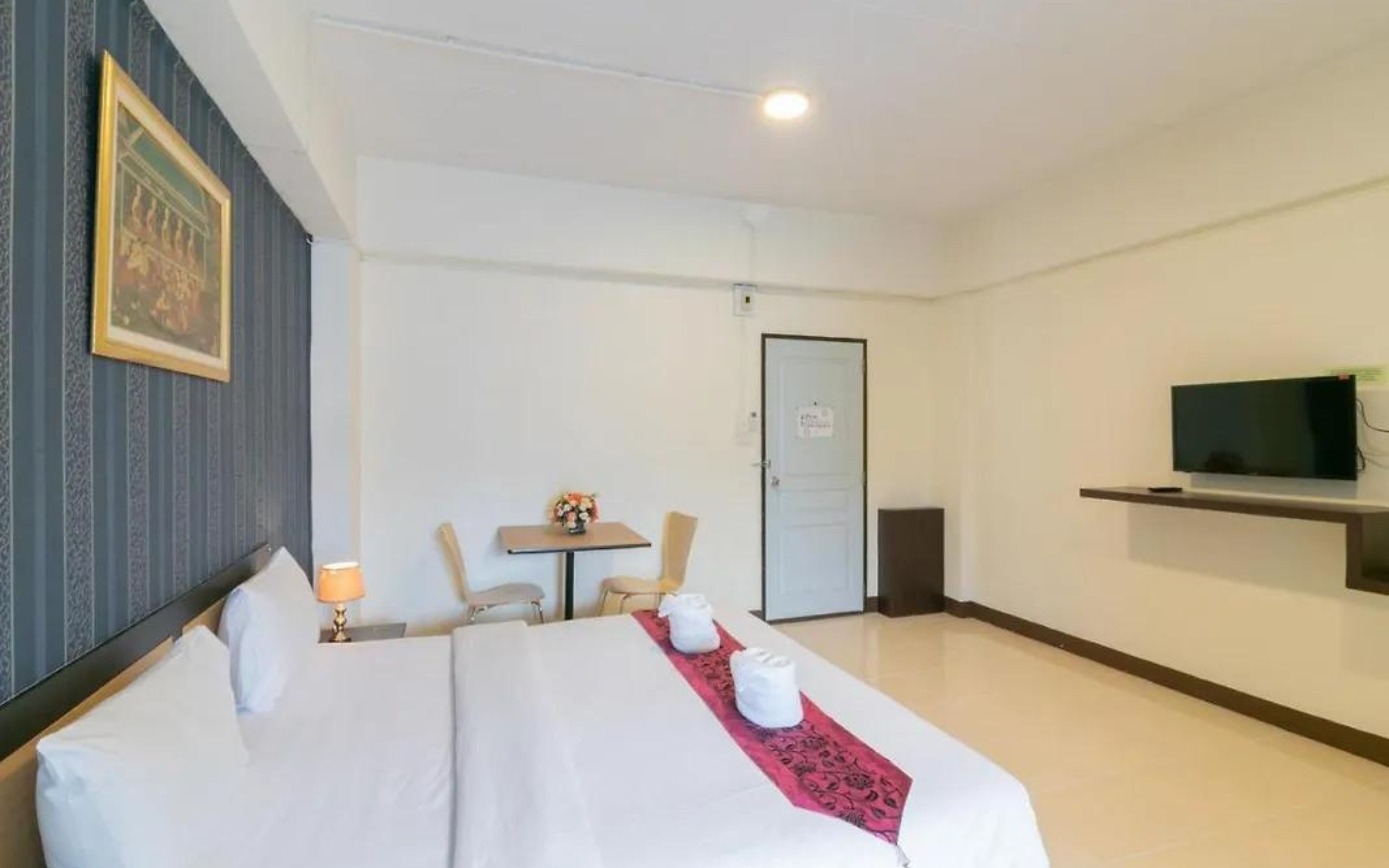 A hotel room with a bed, a desk, a chair, a television, and a door.