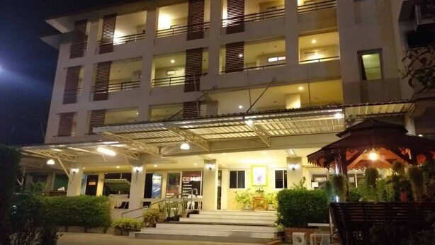 Et hotel med flere etager, overdækket indgang, udendørs siddepladser og krukkeplanter.