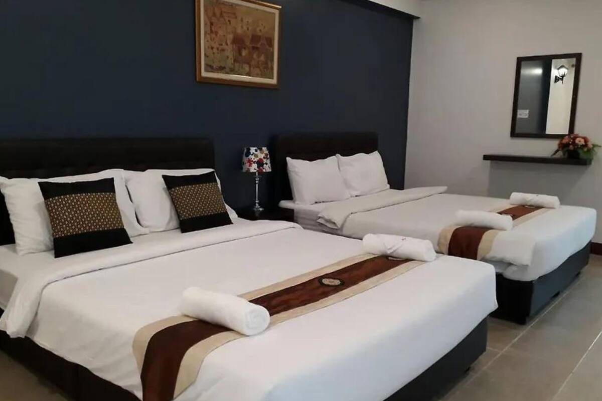 A hotel room with two beds, each with white linens and decorative pillows. There is a framed picture on the wall above the beds and a mirror on the wall to the right.