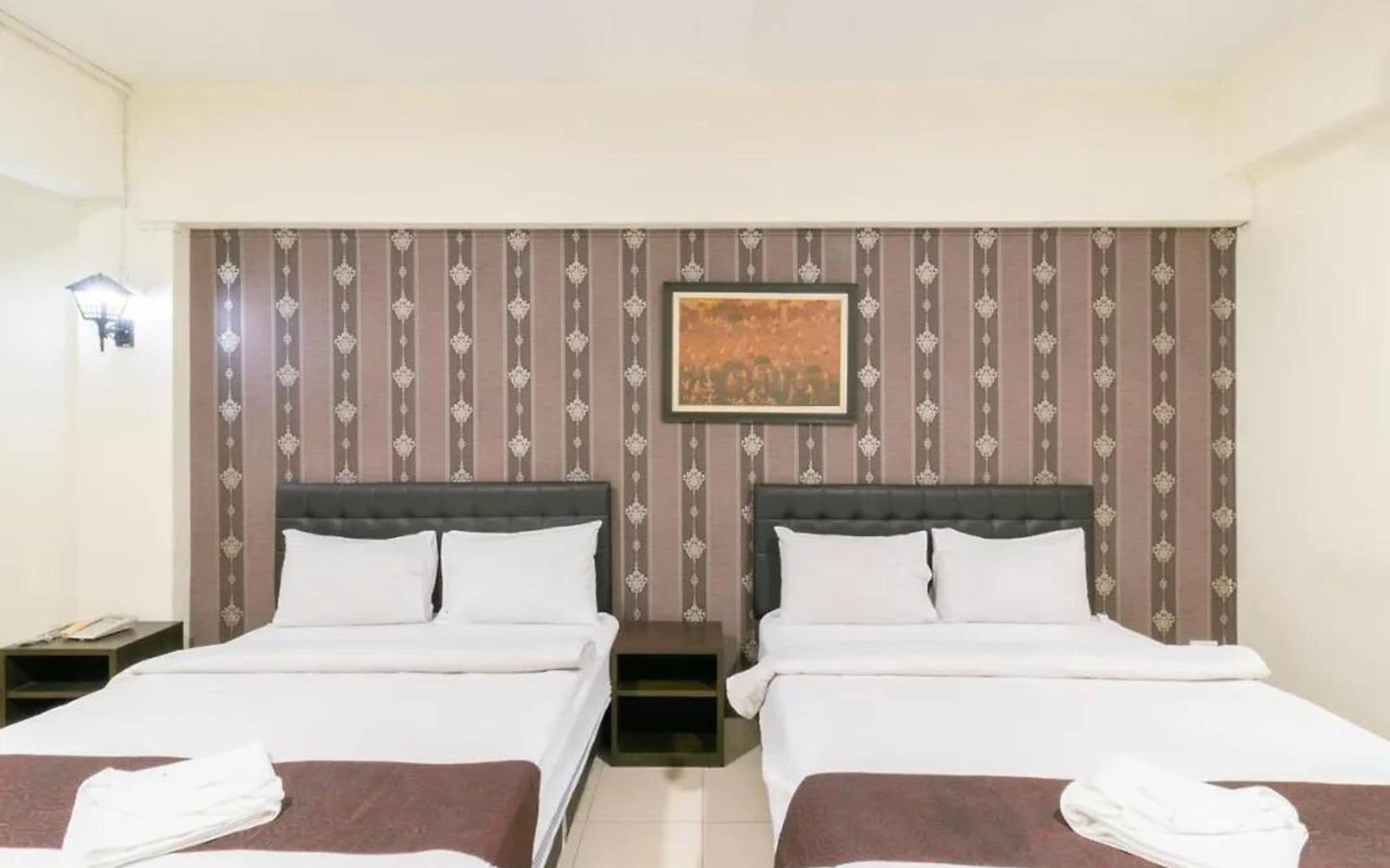 A hotel room with two beds, a nightstand, a framed picture on the wall, and a lamp.