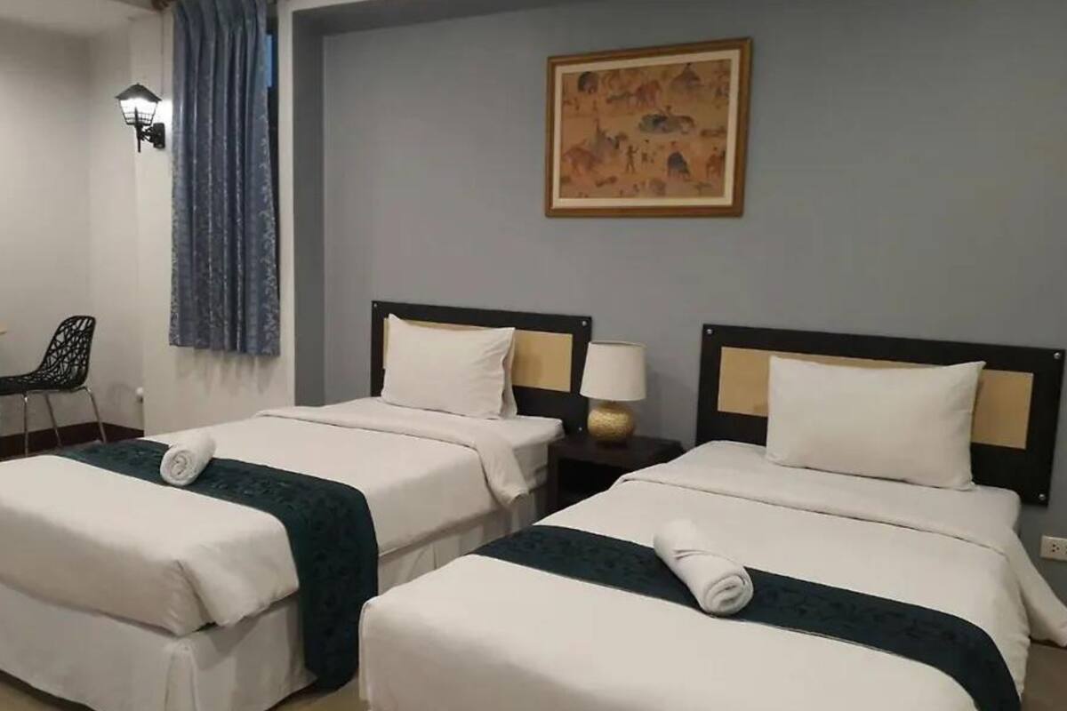 A hotel room with two single beds, a desk with a chair, a lamp, and a painting on the wall.