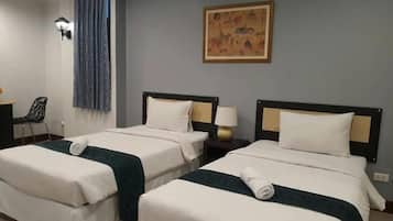 Une chambre d’hôtel avec deux lits simples, un bureau avec une chaise, une lampe et un tableau au mur.