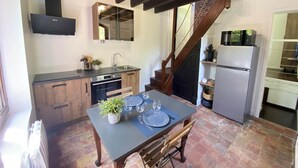 A compact kitchen with a dining table set for four, a built-in oven, and a refrigerator. - La Maison du Garde (STE OPPORTUNE LA MARE)