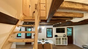 A wooden loft bedroom with a staircase, a dining area with a table and chairs, and a kitchen area with cabinets and a TV. - La Chaumine ` (STE OPPORTUNE LA MARE)