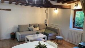 A cozy living room with a sofa, a small table, and a window with a view of greenery. - La Chaumine ` (STE OPPORTUNE LA MARE)
