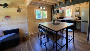 Interior acolhedor de cabana com zona de refeições em madeira, cozinha compacta e sofá.