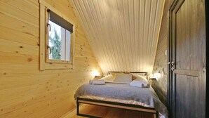 Um quarto de madeira com teto inclinado, uma cama com almofadas e um cobertor, uma janela e uma porta.