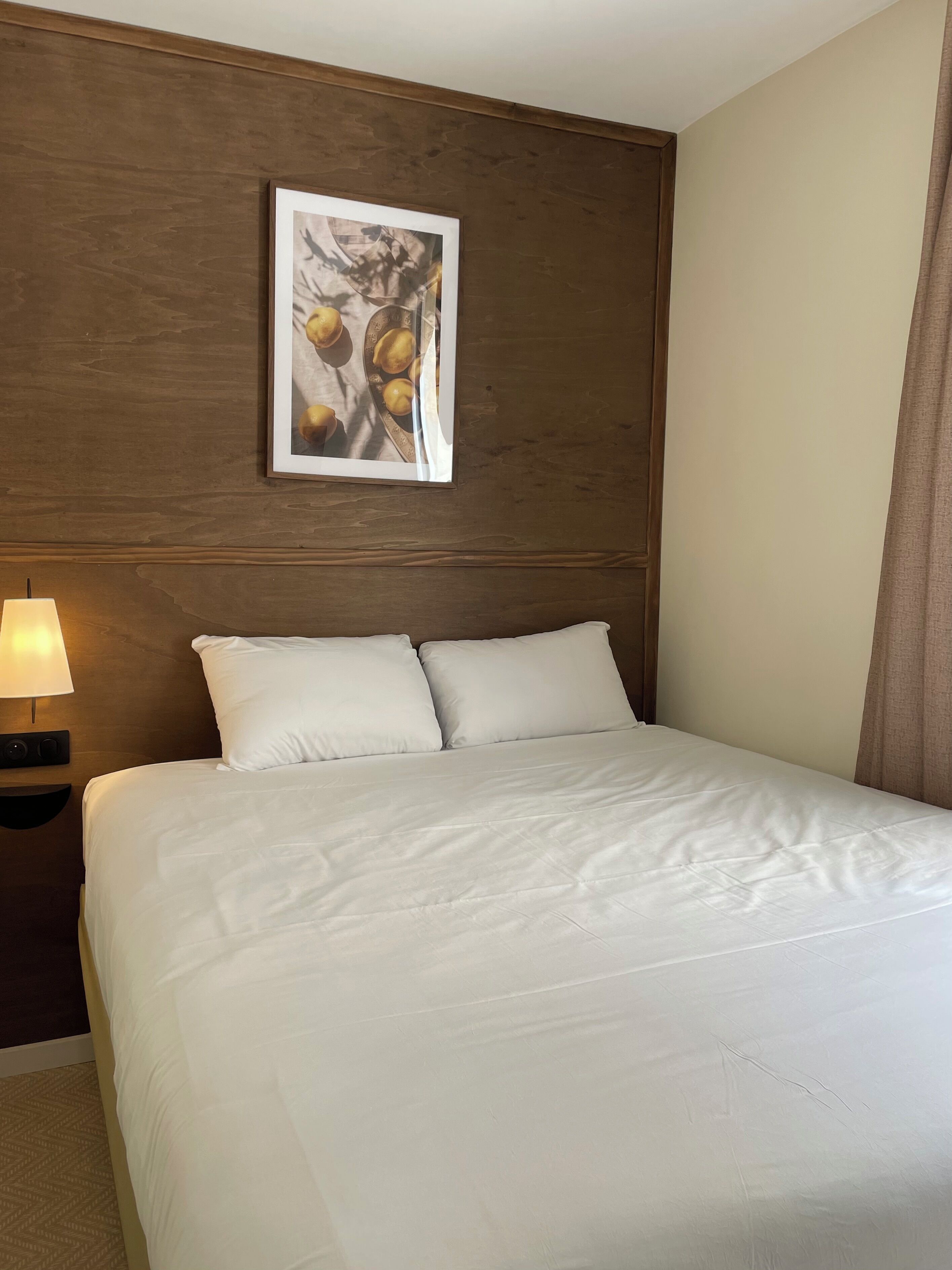 Una habitación de hotel con cama, mesita de noche con lámpara y un cuadro en la pared.