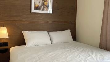 Una habitación de hotel con cama, mesita de noche con lámpara y un cuadro en la pared.