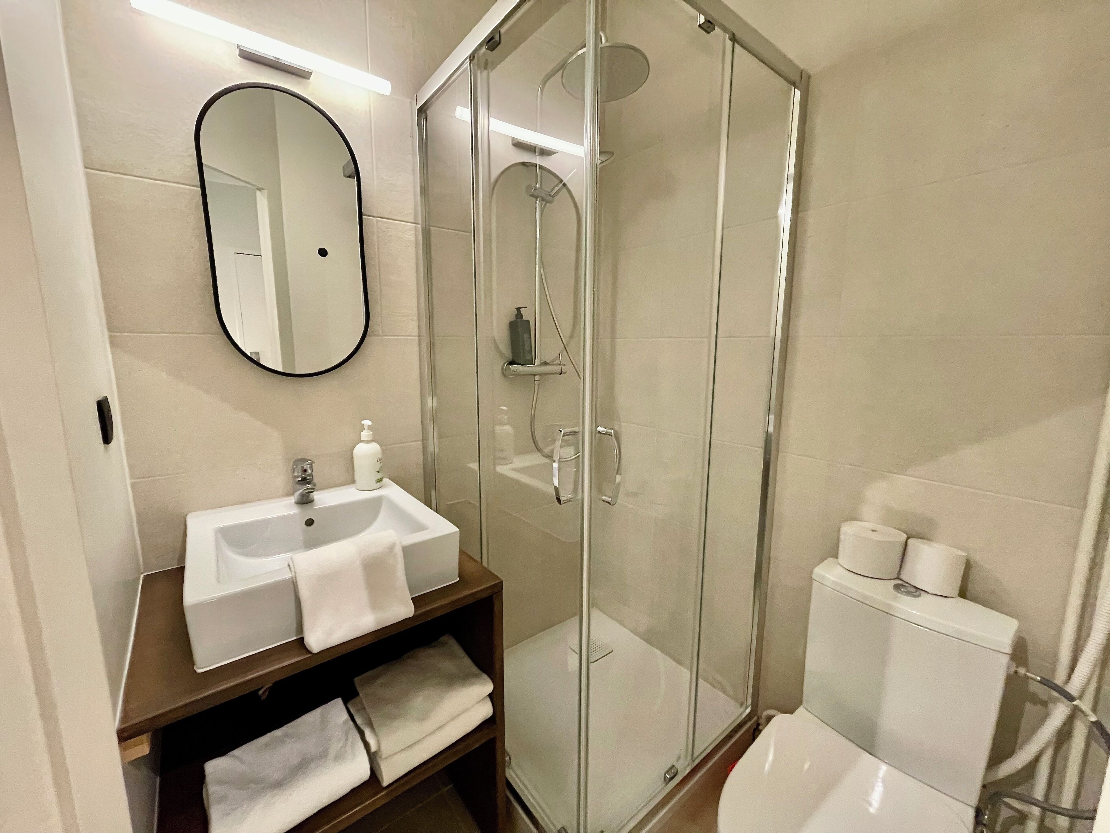 Ein modernes Badezimmer mit einer Glaskabine zur Dusche, einem weißen Waschbecken mit Spiegel und einer Toilette.