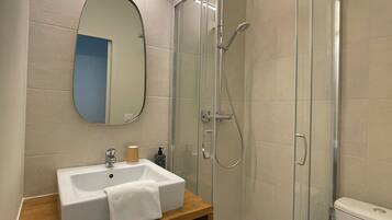 A bathroom with a glass-enclosed shower, a sink with a mirror, and a toilet.