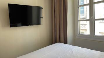 Quarto com cama, televisão de tela plana na parede e janela com cortinas.