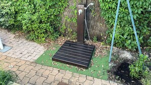A portable shower with a metal grate, a hose, and a control panel, set against a backdrop of dense green foliage. - Villa, Plein Coeur du Moulleau-arcachon, 8 Personnes (Arcachon)