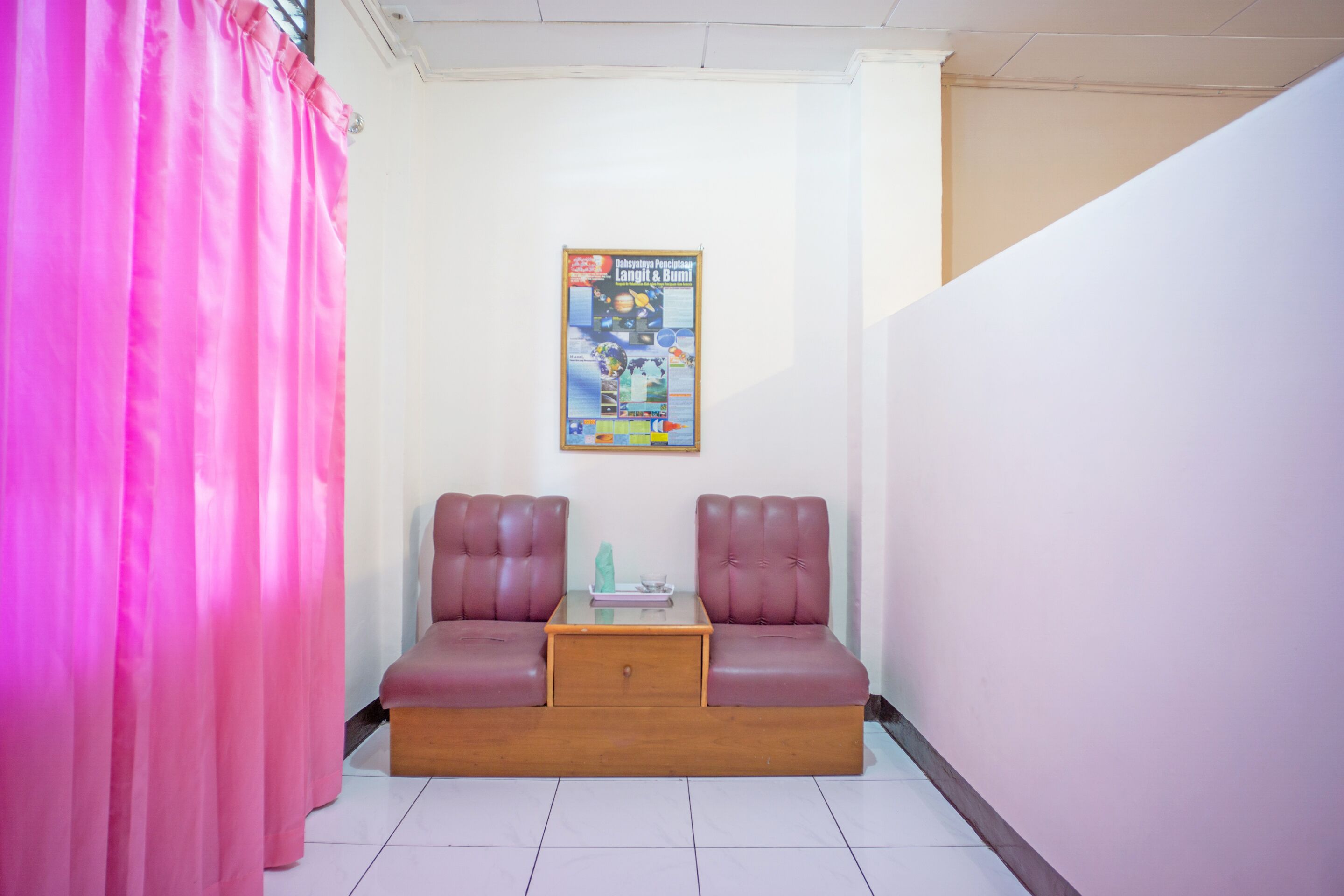 A room with a pink curtain, a poster on the wall, and a sofa with a small table in front.