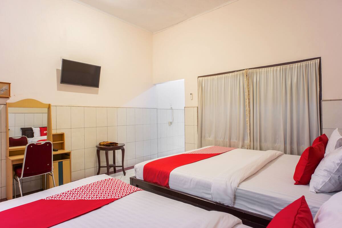 Ein Hotelzimmer mit zwei Betten, einem Schreibtisch, einem Stuhl, einem Fernseher und einem Fenster mit Vorhängen.