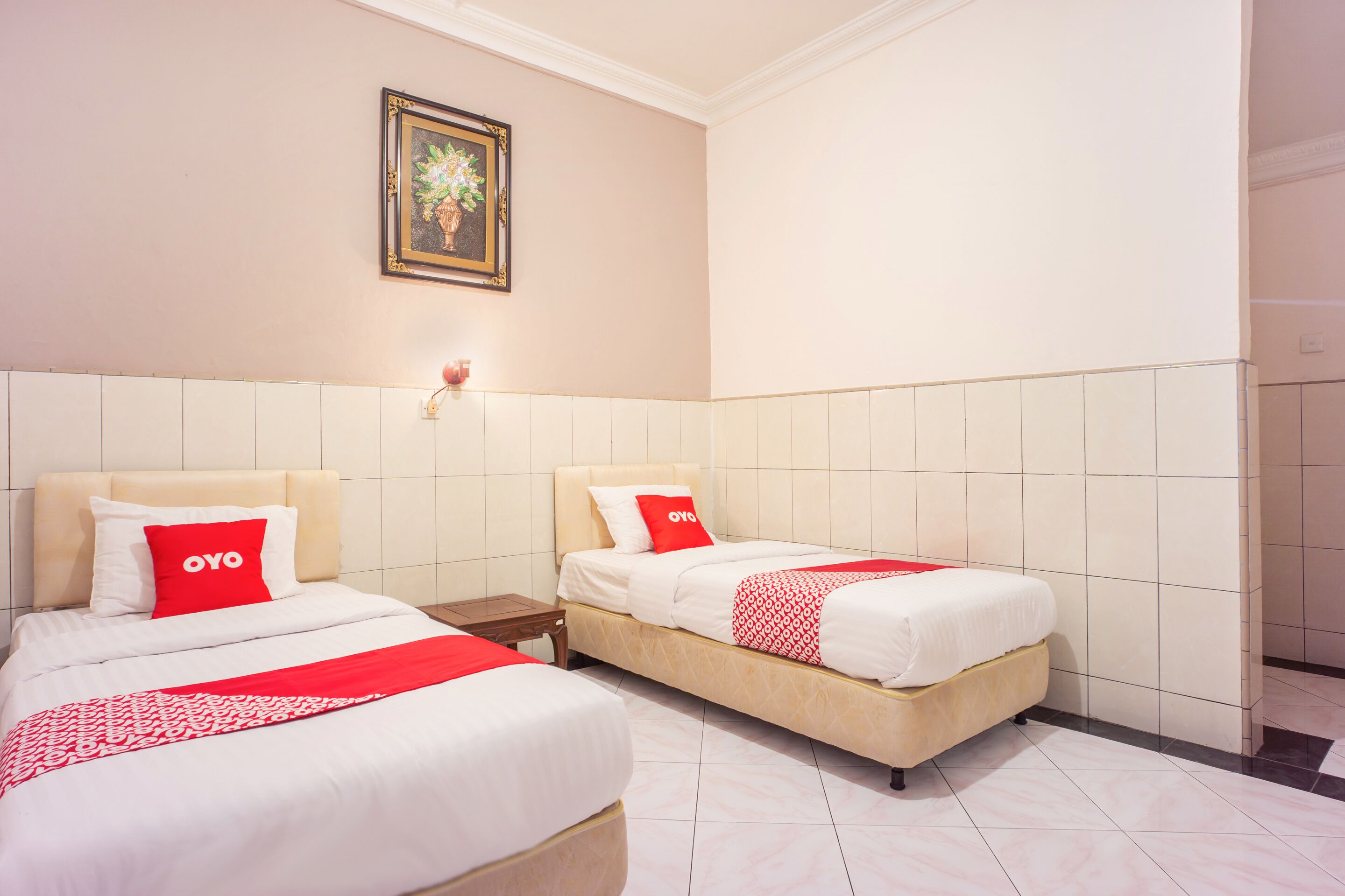 A hotel room with two beds, each with a red OYO branded pillow, a white bedspread, and a red and white patterned throw.