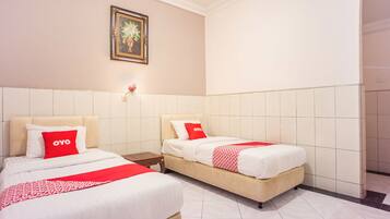 A hotel room with two beds, each with a red OYO branded pillow, a white bedspread, and a red and white patterned throw.