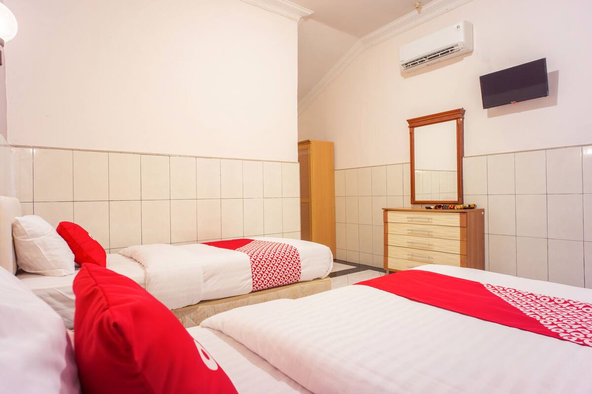 Ein Hotelzimmer mit zwei Betten, einem Holzkapstativ, einem Spiegel, einer Klimaanlage und einem Fernseher.