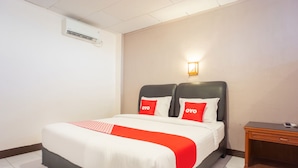 A hotel room with a bed, a bedside table, a wall-mounted air conditioner, and a wall-mounted light fixture. - OYO 2180 Vina Vira Hotel (Lhokseumawe)