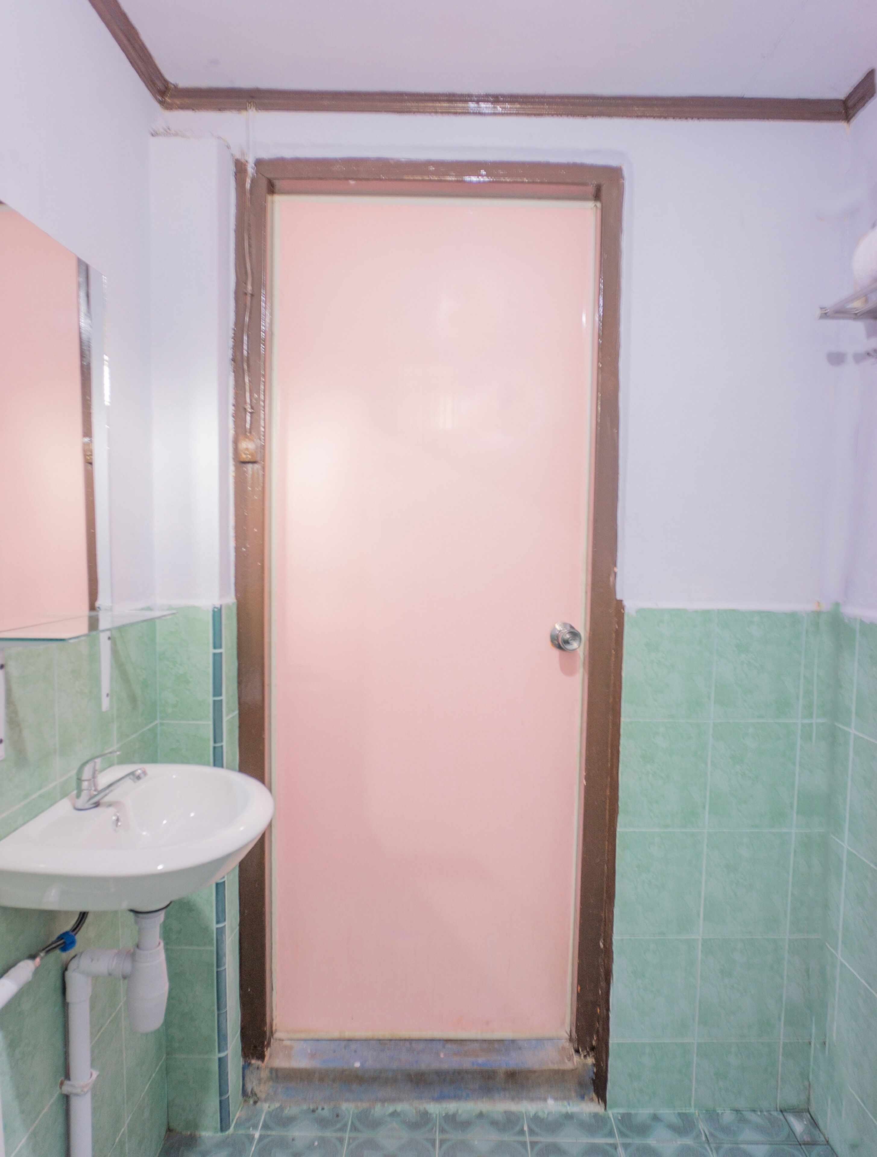 A bathroom with a pink door, a white sink, and green tiled walls.
