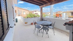 A covered patio with a round table and chairs, a tiled floor, and a view of surrounding buildings. - H 51 FAMILY HOUSE  (Budoni)