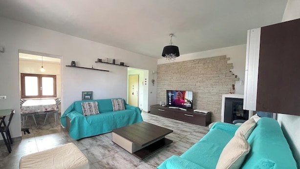 A modern living room with a sofa, a coffee table, and a TV. There is a brick wall and a window with blinds. - H 51 FAMILY HOUSE  (Budoni)