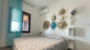 A bedroom with a bed, a window with curtains, an air conditioning unit, and wall-mounted hats. - H 51 FAMILY HOUSE  (Budoni)