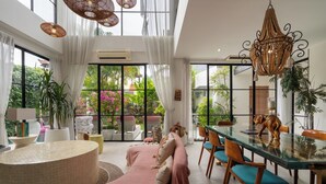 A spacious living area with a glass dining table, comfortable seating, and a view of lush greenery outside. - Maison Jolie Villa by Betterplace (Canggu)