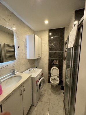 A modern bathroom with a sink, washing machine, toilet, and a glass shower enclosure. - Istanbul Relax Suite (Istanbul)