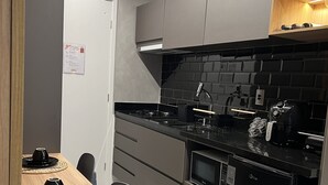 Eine moderne Küche mit grauen Schränken, einer schwarzen Arbeitsplatte und einem eingebauten Ofen. Ein Esstisch mit schwarzen Tellern und einem Stuhl sind ebenfalls vorhanden.