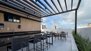 Eine Terrasse im Freien mit Barbereich, Sitzgelegenheiten und Blick auf die Skyline der Stadt.