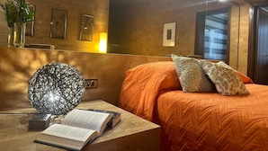 Un dormitorio con una cama grande, una mesita de noche con un libro, una lámpara decorativa y cuadros en la pared.