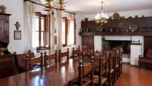Un comedor con una larga mesa de madera y sillas, una lámpara de araña y una chimenea.