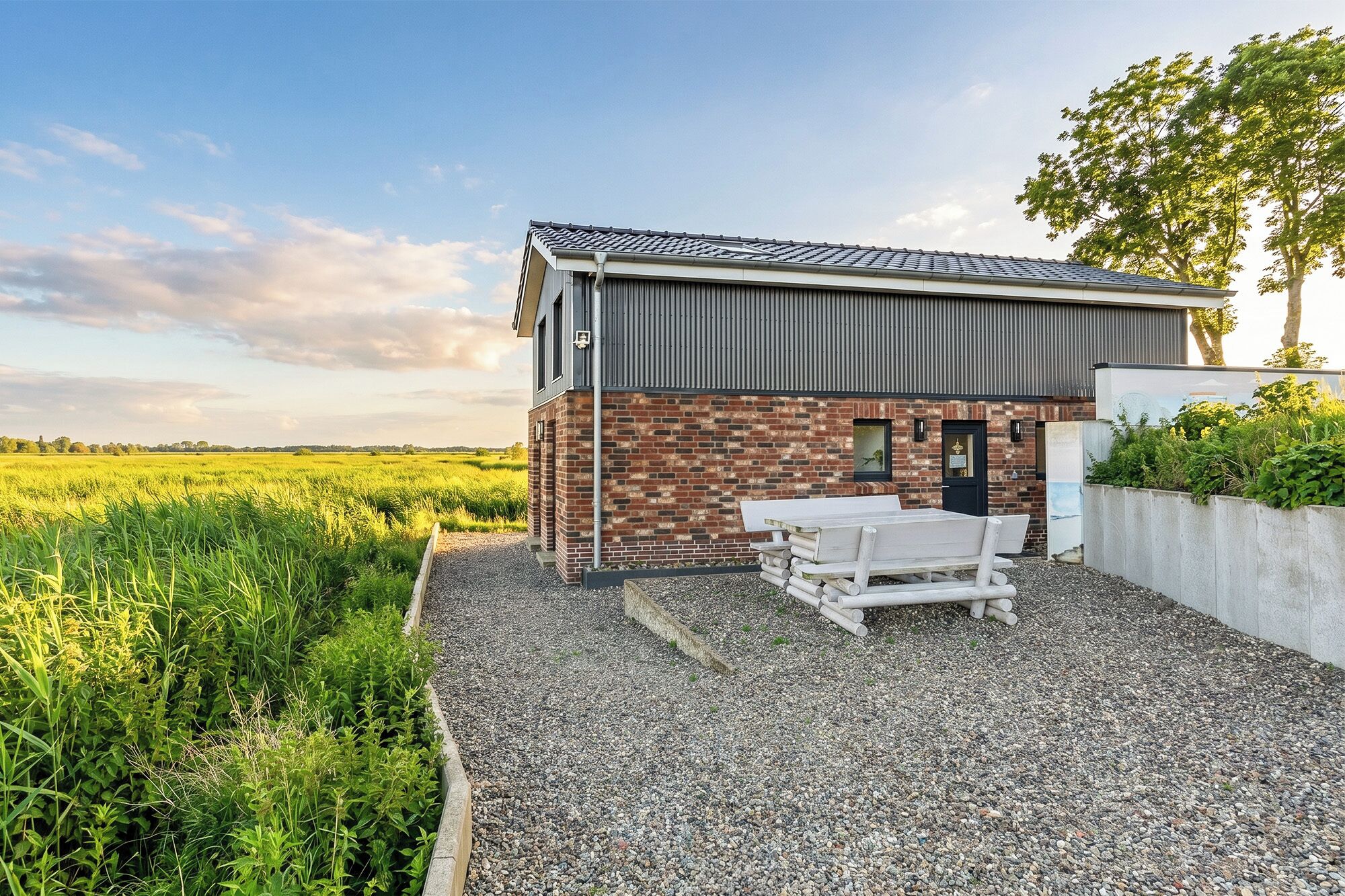 A modern building with a brick facade, a flat roof, and a gravel patio with a wooden bench.