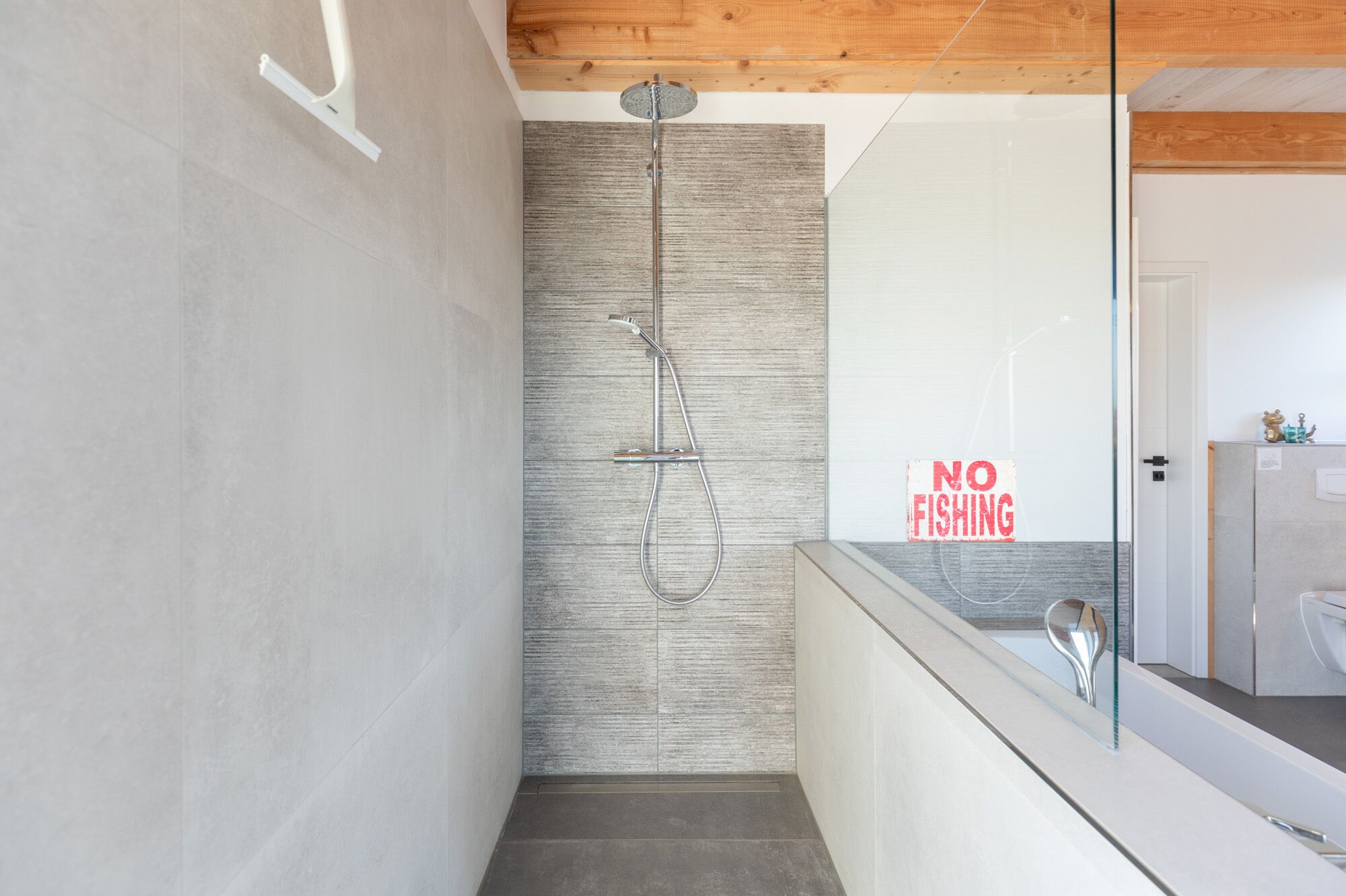 A modern bathroom with a shower, a 'NO FISHING' sign, and a wooden ceiling.