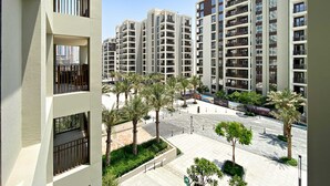 A modern apartment complex with multiple high-rise buildings, a central courtyard with palm trees, and a clear blue sky. - Silkhaus Surf 1 Dubai Creek Harbour (Dubai)
