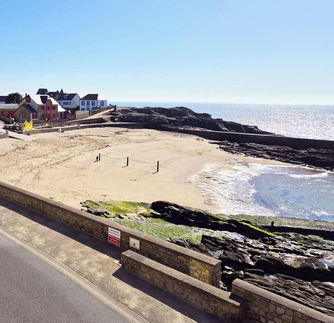 A coastal promenade with a sandy beach, stone walls, and a clear view of the sea.