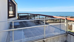 A balcony with a view of the sea, a glass railing, and a concrete floor.